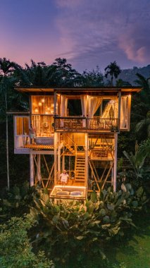 Canlı tropikal yaprakların arasında eşsiz bir bambu ev alacakaranlık gibi sıcacık parlıyor. Büyüleyici mimarisi ve büyüleyici manzarası Bali, Tayland 'da huzur ve macerayı çağrıştırıyor..