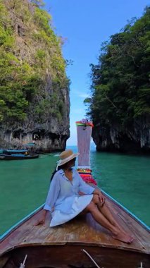 Bir kadın, Tayland 'daki çarpıcı kireçtaşı uçurumları ve turkuaz sularıyla çevrili geleneksel uzun kuyruklu bir teknede dinleniyor. Koh Hong Adası bu tropik cennetin canlı renkleri..