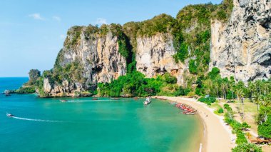 Turkuaz sular Railay Sahili 'nin kumlu sahillerinde yavaşça dolaşırken kayıklar kıyı şeridi boyunca süzülüyor. Bereketli yeşillik, açık mavi gökyüzünün altında yükselen kayalıklarla buluşarak Krabi 'de barışçıl bir kaçış yaratıyor..