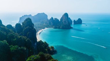 Railay Sahili 'nin sakin suları, Krabi Tayland' ın büyüleyici kireçtaşı kayalıkları tarafından çerçevelenmiş parlak güneşin altında parıldıyor.