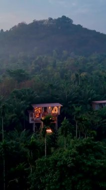 Tayland 'da sık orman yapraklarıyla çevrili sakin bir saklanma yeri deneyimi. Geri çekilmenin sıcaklığı, alacakaranlık çöktükçe huzurlu bir atmosferi yansıtıyor..