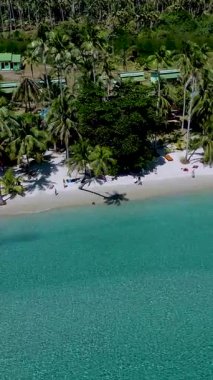 Parlak turkuaz sular, Koh Kood Tayland 'da sallanan palmiyelerle kaplı sakin bir plaja nazikçe sarılır. Ziyaretçiler güneşli gökyüzünün altındaki sakin atmosferin tadını çıkarıyorlar.