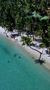 Plaja gidenler sakin bir tropikal ortamda güneşli bir günün tadını çıkarırken yumuşak dalgalar yavaşça kıyıya vuruyor. Rüzgarda sallanan palmiyeler Koh Kood Tayland 'da dinlenmek için sakin bir atmosfer yaratıyor.