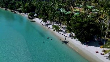 Güneş banyosu yapanlar sallanan palmiye ağaçlarıyla çevrili beyaz kumda dinlenirken dalgalar yavaşça kıyıya çarpar. Tropik cennet Koh Kood Tayland kıyıları boyunca sükunet ve keşfe davet ediyor.