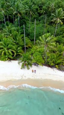 İki ziyaretçi, canlı yeşillik ve berrak sularla çevrili Koh Kood Adası Tayland 'ın sakin kıyı şeridi boyunca yürüyor..