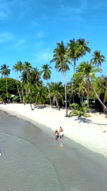 Tayland 'daki Koh Kood Adası' nın el değmemiş beyaz kumlarında güneşin altında rahatla. Dalgalar kıyı boyunca gezerken ziyaretçiler, bereketli palmiye ağaçları ve açık mavi gökyüzü ile çevrili..