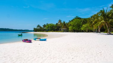 Ziyaretçiler, turkuaz sular ve yemyeşil yemyeşil yemliklerle çevrili el değmemiş Koh Kham Adası Tayland plajında sakin bir günün tadını çıkarıyorlar. Kanolar açık mavi gökyüzü altında maceraperestleri bekliyor..