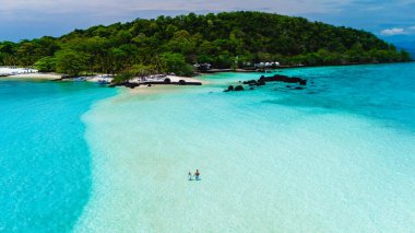 Tayland 'daki Koh Kham Adası' nın nefes kesici turkuaz sularının ve yumuşak kumlu sahillerinin tadını çıkarın. Ziyaretçiler açık gökyüzünün altında kıyı şeridini keşfederek pitoresk bir tropikal kaçış yaratıyorlar..