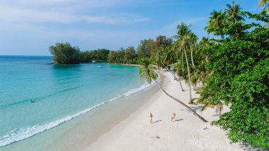 Parlak güneş ışığı, iki yolcunun kıyı boyunca yürüdüğü Koh Kood Adası 'nın el değmemiş kumlu plajını aydınlatır. Bereketli palmiye ağaçları sakin sahneyi çevreleyerek rahatlamaya ve keşfetmeye davetiye çıkarır..