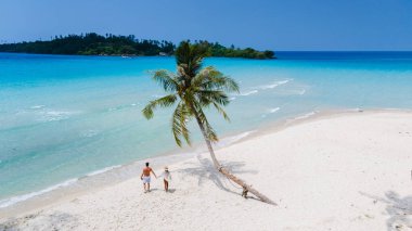 Tayland 'daki Koh Kood Adası' nda güzel bir sahil hayal edin. Bir çift palmiye ağaçlarının altında el ele dolaşır, turkuaz suların ortasında romantik bir tatil ortamı yaratır.