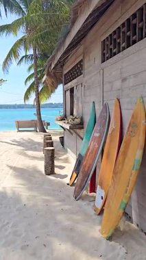Tayland 'da bulunan Koh Kham Adası' ndaki ahşap bir kulübede renkli sörf tahtaları duruyor. Kumlu sahil ve berrak mavi su rahatlama ve su sporları için mükemmel bir ortam yaratır..