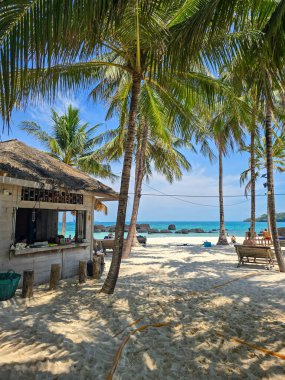 Tayland 'ın Koh Kham Adası' ndaki sakin bir plajda sallanan palmiye ağaçları ve yumuşak kumlu kıyılar bulunur. Sakin turkuaz su, ziyaretçileri güneşlenmeye ve cennette dinlenmeye davet ediyor..