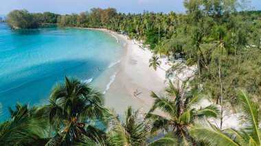 Tayland 'daki Koh Kood Adası' nın sakin kıyı şeridi, yumuşak beyaz kum, kristal berrak su ve sallanan palmiye ağaçları. Ziyaretçiler huzurlu atmosfer ve doğal güzelliğin tadını çıkarıyorlar..