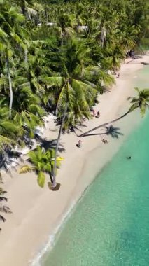 Ziyaretçiler, bereketli palmiye ağaçları ve zümrüt sularıyla çevrili Koh Kood Tayland 'da sakin bir sahilde güneşli bir günün tadını çıkarıyorlar. Güneş banyosu yapanlar ve kayakçılar doğal güzellik ve sıcaklıktan zevk alırlar..