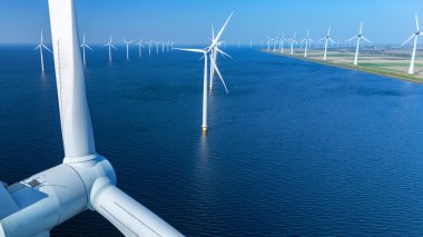 Sakin sulara yayılan yel değirmeni türbinleri Hollanda 'nın berrak gökyüzüne karşı dimdik ayakta duruyor. Açık denizlerdeki yel değirmeni türbinleri Hollanda 'daki yeşil enerji geçişinde