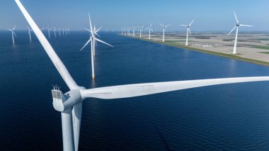 Hollanda açıklarındaki yel değirmeni parkında açık mavi gökyüzüne karşı sayısız rüzgar türbini temiz enerji üretiyor. Offshore yel değirmeni türbinleri okyanusta yeşil enerji geçişinde