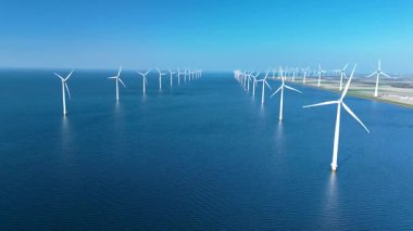 Hollanda kıyıları açıklarında temiz enerji üreten, sakin sularda geniş bir rüzgar türbini dizisi yüksekte duruyor. Okyanustaki yel değirmeni türbinleri, yeşil enerji geçişi