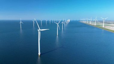 Açık denizlerdeki geniş rüzgar türbinleri açık mavi gökyüzüne karşı dik durarak Hollanda kıyı şeridi boyunca temiz enerji üretiyor. Bu yenilenebilir enerji kaynağı yenilik ve sürdürülebilirliği temsil etmektedir.