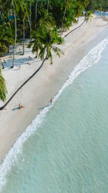 Tayland 'daki Koh Kood Adası' nın sakin güzelliğini tecrübe edin. Yumuşak beyaz kumların berrak turkuaz sularla buluştuğu yer. Palmiyeler usulca sallanıyor kumsala gidenler gibi güneşin altında huzurlu bir günün tadını çıkarıyorlar..