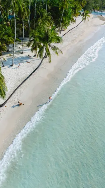 Tayland 'daki Koh Kood Adası' nın sakin güzelliğini tecrübe edin. Yumuşak beyaz kumların berrak turkuaz sularla buluştuğu yer. Palmiyeler usulca sallanıyor kumsala gidenler gibi güneşin altında huzurlu bir günün tadını çıkarıyorlar..