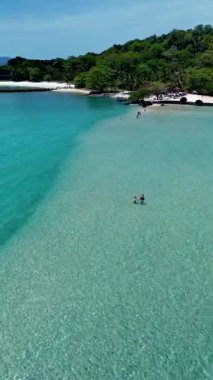 Koh Mak ve Koh Kham Adası 'nın güzelliğinin tadını çıkarın. Tayland' da yemyeşil ve canlı plajlarla çevrili saydam sularda yürüyen iki insan.