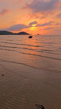 Güneş Koh Mak adalarının sakin sularında batarken altın renkler gökyüzünü dolduruyor. Tayland 'da bir tekne ufukta huzur içinde sürüklenirken, dalgalar kıyıları okşuyor.
