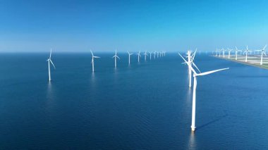 Hollanda 'da sayısız rüzgar türbininin bulunduğu geniş bir yel değirmeni parkının panoramik manzarası. Mavi sular temiz enerji teknolojisiyle tezat oluşturarak alternatif enerji çözümlerini destekliyor..