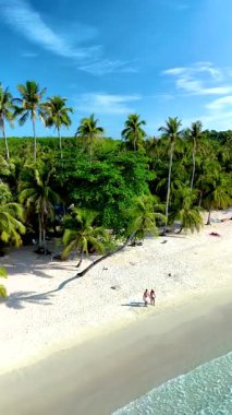 İki kişi, Tayland 'ın el değmemiş Koh Kood Adası sahilinde, gür palmiye ağaçlarıyla çevrili, huzurlu bir yürüyüşün tadını çıkarıyor. Parlak mavi gökyüzü ve davetkar kumlar mükemmel bir tropikal kaçış yaratır..