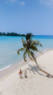 Tayland 'daki Koh Kood Adası' nın çarpıcı ve dingin güzelliğini bu resimli plaj sahnesiyle yakalayın. Gün batımında sallanan palmiye ağaçlarının altında güzel bir aile gezintisi.