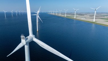 Hollanda 'daki açık deniz yel değirmeni parkının geniş bir görüntüsünde çok sayıda rüzgar türbini jeneratörü yenilenebilir enerjiden faydalanıyor. Sakin sular sakin bir atmosfere katkıda bulunur..