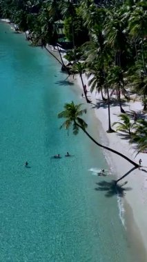 Güneş ışığı turkuaz suları yansıtıyor. İnsanlar kumlu sahilde boş zaman aktivitelerinin keyfini çıkarıyorlar. Palmiyeler hafifçe sallanıyor, Koh Kood Tayland 'da rahatlamak ve eğlenmek için mükemmel bir tropik cennet yaratıyor..