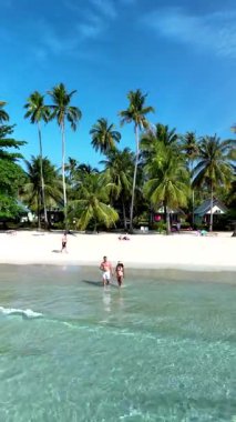 Yumuşak kumların berrak sularla buluştuğu Koh Kood Adası Tayland 'ın doğal güzelliğini keşfedin. İki insan, bereketli palmiye ağaçlarıyla çevrili kıyı boyunca sakin bir şekilde yürümekten zevk alır..