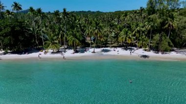 Güneşli bir günde Koh Kood Tayland 'da ziyaretçilerin bereketli palmiye ağaçları ve kristal berrak sularla çevrili beyaz kumlar boyunca yürüdüğü ve rahatlamak için mükemmel bir kaçış atmosferi yarattığı güneşli bir sahil..