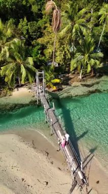 Nefes kesici bir tropikal dekor, Koh Kood Tayland 'daki kristal berrak turkuaz su üzerinde uzanan kırsal ahşap bir köprüyü içerir.