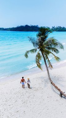 Koh Kood Adaları kumlu kumsalında, turkuaz sular ve yemyeşil sularla çevrili, Tayland 'da cennette huzurlu ve romantik bir anın tadını çıkaran güzel bir çift el ele yürüyor.