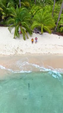 Tayland 'daki Koh Kood Adası' nın güzelliğini keşfedin. İki insan el değmemiş kumsalda, sallanan palmiye ağaçları ve gök mavisi sularıyla çerçevelenmiş sakin bir gezinti yaparken..