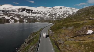 Norveç 'in engebeli dağlarının dingin güzelliğini keşfedin. Bir karavan, parlayan bir gölün yanındaki dolambaçlı bir yolda ilerliyor. Geiranger Norveç yakınlarındaki Langvatnet yolunda bir kamp aracı.