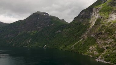 Norveç 'teki Geiranger fiyortunun nefes kesici güzelliğini keşfedin, yüksek dağlar ve yemyeşil bitkilerle çevrili. Sakin sular bu resmedilmiş ortamın doğal ihtişamını yansıtıyor..