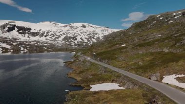 Kristal berrak sular, Norveç 'in dağlık arazisindeki büyüleyici kar örtülü zirveleri yansıtır. Dolambaçlı bir yol, Geiranger Norveç yakınlarındaki Langvatnet yolunda gezginleri gezmeye davet ediyor.