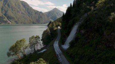 Norveç 'te sakin bir göl kenarında dolambaçlı bir yol. Bereketli yeşillik manzarayı çerçeveler, muhteşem dağlar arka planda yükselir, Fjaerlandsfjorden, Sognefjord Norveç yolcuları için barışçıl bir kaçış yaratır