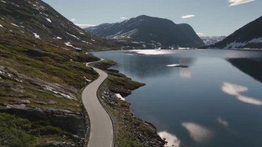 Norveç 'te dolambaçlı bir yol boyunca nefes kesen bir yolculuk, heybetli dağlarla çevrili ve gökyüzünü yansıtan sakin bir göl. Doğal güzellik her gezgini cezbeder..