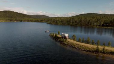 Norveç 'te sakin bir gölün dinginliğini hissedin, rahat bir karavan yüksek ağaçların arasında dururken, bir tekne sakin sularda süzülüyor, doğanın güzelliğinin tadını çıkarıyor..