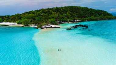 Turkuaz sular yumuşak kumlu kıyılara nazikçe yaklaşırken sahile gidenler Koh Mak ve Koh Kham Adası yakınlarındaki Tayland 'ın dingin güzelliğinin tadını çıkarıyorlar. Yeşillik kıyı şeridi, huzurlu bir kaçış yaratıyor..