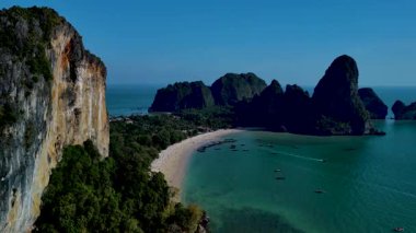 Krabi Tayland 'ın gök mavisi sularında süzülen manzara, muhteşem uçurumlar, sakin plajlar ve parlak gün ortası güneşi altında yavaşça sürüklenen tekneler sergiliyor.
