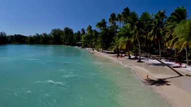 Beyaz kumlar Koh Kood Tayland tropikal limanında turkuaz sularla buluşur. Bereketli palmiye ağaçları yavaşça sallanırken, güneşlenenler sakin kıyı şeridi boyunca sıcak güneş ışığının tadını çıkarıyorlar.