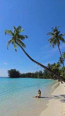 Koh Kood Tayland 'da sakin bir plajın berrak mavi suları boyunca sallanan palmiye ağaçlarının altında dinleniyor. Güneş parlıyor, tropikal atmosferi ve rahatlığı arttırıyor..