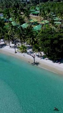 Güneş ışığı kristal berrak sularda parlarken, ziyaretçiler, sallanan palmiyelerle dolu el değmemiş bir plaj boyunca yürüyorlar. Koh Kood Tayland 'daki bu tropikal vahayı yemyeşil alan kaplar..