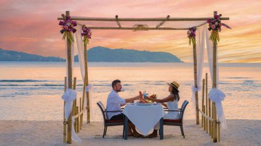 Phuket Tayland 'da, orta yaşlı bir çift sahilde romantik bir akşam yemeği yiyor. Batan güneş, gökyüzünü sıcak renklerle boyuyor. Lüks tatilleri için büyülü bir atmosfer yaratıyor..