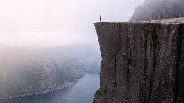 Norveç 'te şafak sökerken Lysefjord' un nefes kesici manzarasını emen yalnız bir figür Preikestolen 'in kenarında duruyor.