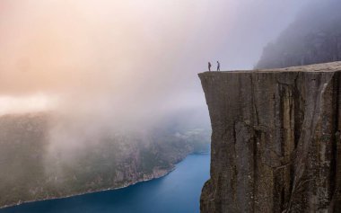 Norveç 'te görkemli bir uçurum olan Preikestolen' in kıyısında iki figür duruyor. Etrafı sisle çevrili nefes kesici manzara, keşif ve huşu uyandıran çarpıcı bir atmosfer sunuyor..